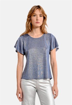 Top corto blu lucido con una vestibilità ampia e scollatura rotonda, caratterizzato da un tessuto leggermente testurizzato. Abbinato a pantaloni metallici argentati.