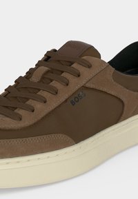 Baskets en daim et cuir marron avec lacets marron foncé et logo "BOSS" sur le côté, semelle en caoutchouc blanche et doublure intérieure noire.