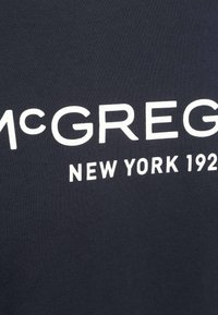 Navyblauwe stoffen t-shirt met gedurfde witte letters: "McGREGOR NEW YORK 1921". Het ontwerp benadrukt een minimalistische stijl.