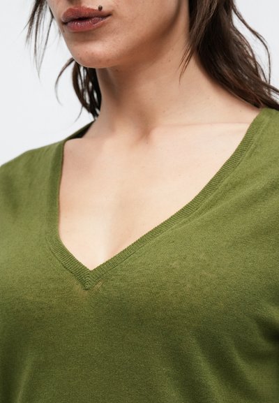 Πουλόβερ ελιάς με βαθύ V λαιμόκοψη, απαλό ύφασμα και εφαρμοστή γραμμή, με ριμπ τελειώματα και ελάχιστες ραφές για καθαρό φινίρισμα.