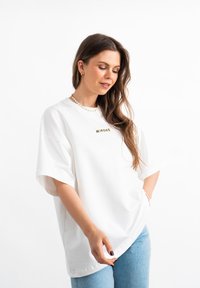 Witte oversized t-shirt met korte mouwen, voorzien van een klein groen "MIRONS" logo op de borst. Gemaakt van zacht katoen met een relaxte pasvorm.