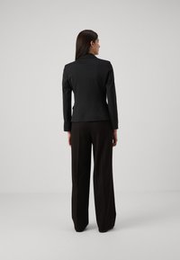 Zwarte op maat gemaakte blazer met gestructureerde schouders, slim fit en een gladde stof, gecombineerd met hoge taille, wijde zwarte broek.