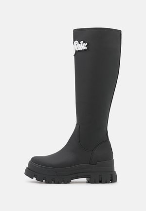 Czarny wysoki do kolana but z grubą podeszwą z bieżnikiem i białą naszywką z logo "Polo" u góry po zewnętrznej stronie.