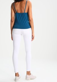 Teal ärmlös topp med tunna band, i kombination med vita skinny jeans och ljusa sneakers. Slät tyg, figurnära design.