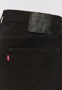 Zwarte denim spijkerbroek met een leren label met merkinformatie, een klein rood label en subtiele stikpatronen op de achterzakken.