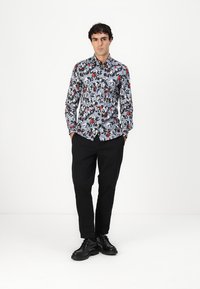 Langermet skjorte med blå bakgrunn, dekorert med et blomsterdesign i rødt, hvitt og svart. Kombinert med svarte bukser og sko.