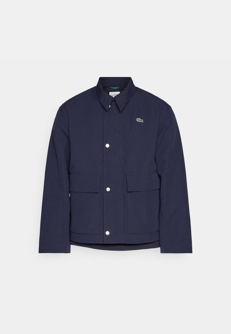 Giacca casual blu navy con colletto, bottoni a pressione, due tasche frontali a pattina e un piccolo logo di coccodrillo verde sul petto.