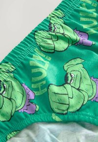 Gröna badbyxor i bomull med serietidningsinspirerade Hulk-grafiker i lila detaljer, med en resårmidja som är rynkad och en slät yta.