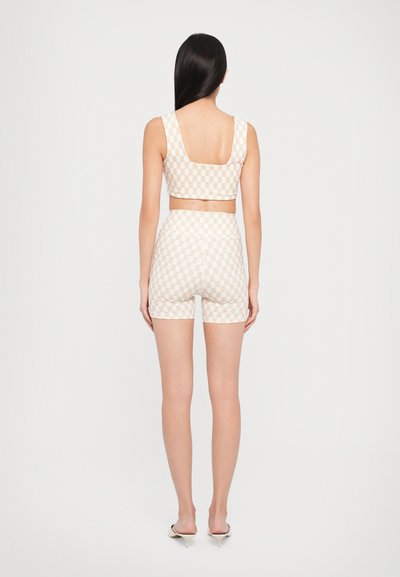 Woman with long dark hair wearing a patterned beige crop top and matching high-waisted shorts, standing with her back facing forward.
