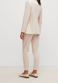 Jasnoróżowa żakiet skrojony na miarę oraz dopasowane spodnie; gładki materiał; dopasowany krój; uzupełnione beżowymi mokasynami i minimalnymi akcentami w hardware.