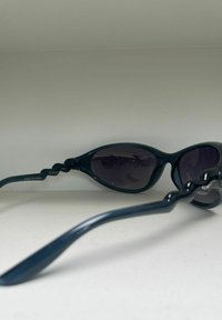 Lunettes de soleil vert foncé avec un design enveloppant, verres teintés et un motif ondulé unique sur les branches. Matériau en plastique léger.