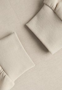 Beige fabric with ribbed cuffs. Smooth texture with subtle soft sheen. Cuffs feature vertical ribbing contrasting the main fabric.