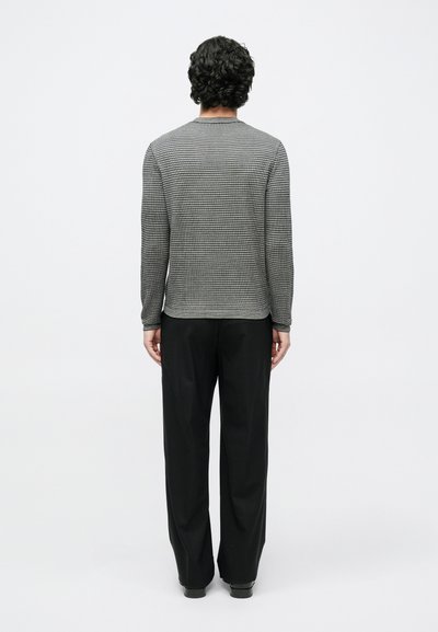 Fekete-fehér mintás hosszú ujjú felső kerek nyakkivágással, fekete bő szárú nadrággal, hátulnézetből.