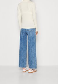 Langemouwen ivoorkleurig shirt, losse blauwe denim wide-leg jeans en witte sneakers met pasteloranje strepen en bruine zolen.