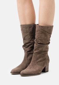 Hnědé semišové kozačky do půli lýtek s volným designem, bočním zipem, zaoblenou špičkou a blokovým podpatkem. Hladká textura a flexibilní střih.
