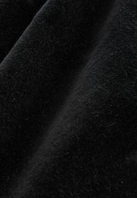 Juodas audinys su minkštu, tekstūruotu paviršiumi, turintis lengvą spindesį ir subtilias skaidulas, sukrautas taip, kad pabrėžtų savo lygų, plaukiantį pobūdį.