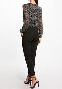 Blusa de lunares en blanco y negro con mangas translúcidas, cintura ajustada y pantalones negros entallados; combinados con sandalias negras de tacón alto con tiras.