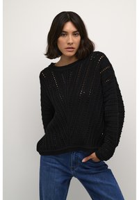 Svart stickad tröja med en texturerad mönster och hålstickning, med rund halsringning och långa ärmar. Matchad med blå denim.