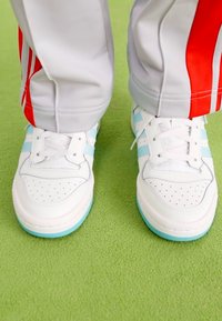 Baltas sporta apavus ar gaiši ziliem akcentiem un perforētiem detaļām. Valkāti ar pelēkiem biksēm ar sarkanām svītrām. Zālei līdzīgs zaļš virsmas segums.