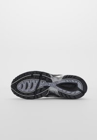 Semelle de chaussure avec motif de bande de roulement noir et gris conçu pour la traction, vue de dessous sur un fond blanc uni.