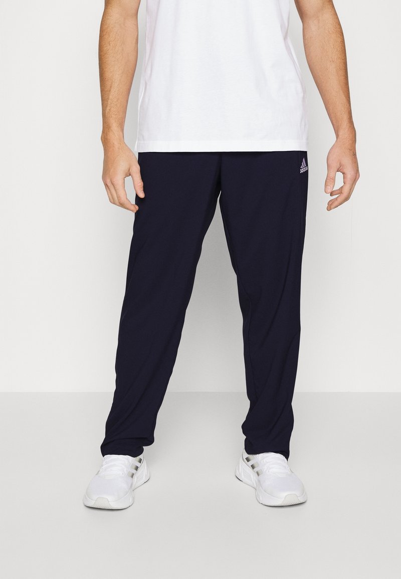 Navy athletic pants with a relaxed fit, featuring an elastic waistband and minimal branding. Paired with white athletic shoes.