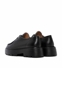 Zapatos de cuero negro con punta redondeada, suela gruesa y estriada, y detalles de costura sutiles en la parte superior. Diseño elegante y moderno.