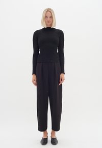 Maglietta nera a maniche lunghe con tessuto testurizzato, colletto alto, abbinata a pantaloni neri larghi e scarpe nere piatte. Design semplice e minimalista.