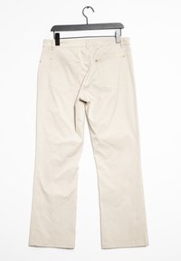 Béžové bavlněné kalhoty vystavené na plocho, s rovnými nohavicemi, dvěma zadními kapsami a zlatými akcenty na okrajích kapes.