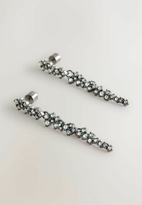 Orecchini in tono argento con un design a cascata, arricchiti da numerosi strass trasparenti che presentano una varietà di forme e una finitura lucida.