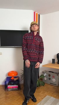 Pullover in pile bordeaux con motivi geometrici, collo con mezza zip e accenti blu navy. Abbinato a pantaloni neri a gamba larga e scarpe nere.