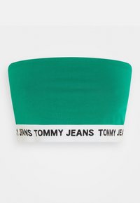 Zelený top bez ramínek vyrobený z hladkého materiálu, s bílým elastickým páskem se zdvojeným černým textem "TOMMY JEANS" podél spodního okraje.