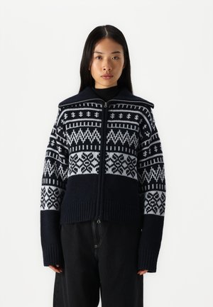Navy a biela pletená cardigan s geometrickými vzormi, so zipsom vpredu, vysokým golierom a rebrovanými manžetami a lemom. Textúrovaný, teplý materiál.