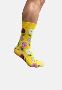 Calcetín de algodón amarillo con un patrón floral que presenta flores rosas, blancas y moradas, hojas verdes y un borde superior acanalado.