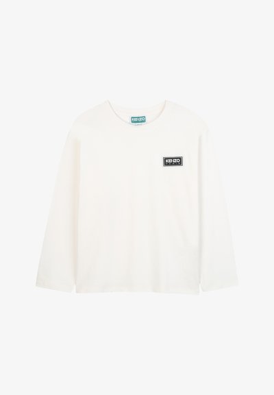 Biała koszulka z długim rękawem z bawełny, z prostokątną czarno-białą naszywką logo na klatce piersiowej, okrągłym dekoltem i luźnym krojem.