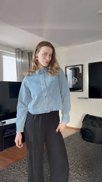 Camisa cropped de ganga azul clara com fecho de botões, mangas compridas e aplicações de pérolas, combinada com calças pretas largas.