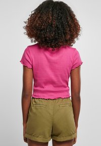 Lilla bomullstopp med korte ermer og bølget nederkant, sammen med olivengrønne bomullsshorts med baklommer og brettede opplegg.