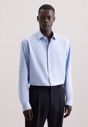 Jasnoniebieska koszula z długim rękawem i jedną kieszenią na piersi, wykonana z miękkiego materiału, w zestawieniu z ciemnymi spodniami.