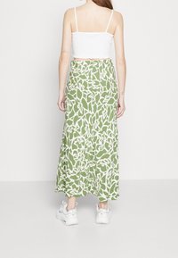 Falda maxi verde con patrón floral blanco; hecha de tela ligera; combinada con una blusa corta blanca y zapatillas blancas.