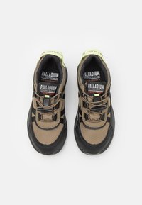 Baskets imperméables avec un design marron clair et noir, dotées d'un dessus texturé, de lacets ajustables et d'un accent vert vif sur le col.