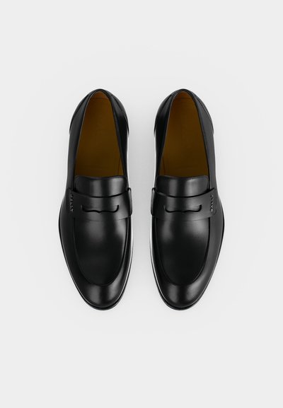 Ζευγάρι μαύρα δερμάτινα loafers χωρίς κορδόνια με στρογγυλεμένες μύτες και χαμηλά τακούνια, εμφανιζόμενα από πάνω σε λευκό φόντο.