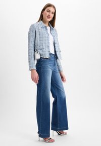 Blauwe tweed cropped jacket met rafelige randen, gedragen over een witte top en gecombineerd met wijde spijkerbroeken. Zilveren hakken en een kleine tas.