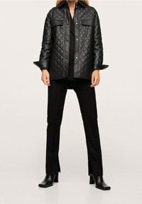 Czarna pikowana kurtka z kieszeniami na klapę, zapięciem na guziki i szerokimi mankietami, w połączeniu z czarnymi spodniami z bocznymi rozcięciami i bootami na kwadratowym nosku.