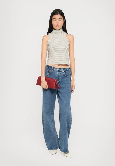 Top smanicato a collo alto a righe in colori chiari, jeans a vita alta blu in denim a gamba larga e una borsa a tracolla rossa. Tacchi a punta bianchi.