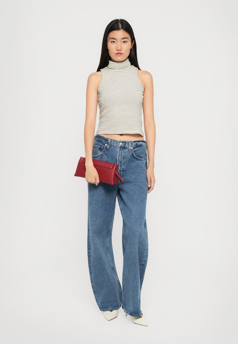Gestreifter ärmelloser Rollkragenoberteil in hellen Farben, hochgeschnittene blaue Jeans im weit geschnittenen Stil und eine rote Clutch. Weiße spitz zulaufende Absatzschuhe.