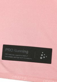 Sort rektangulært mærke på pink stof med teksten "PRO Running" og en bemærkning om højtydende funktionalitet, plus et kluster af seks små cirkler.