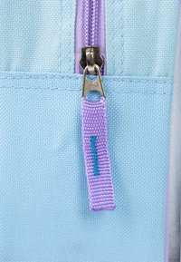 Tessuto azzurro chiaro con una cerniera viola. Il tirante della cerniera è in tessuto testurizzato con un'accento di cucitura turchese.