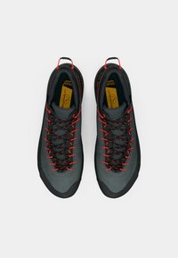 Un par de zapatos de senderismo gris oscuro con cordones naranjas y tiradores, vistos desde arriba sobre un fondo blanco.