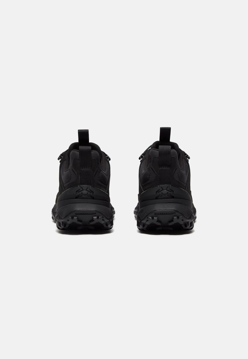 Zapatillas deportivas negras con parte superior texturizada, talón reforzado y suela robusta con patrones de tracción destacados. Dos lengüetas para facilitar el uso.