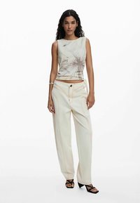 Canotta corta color chiaro con stampa floreale; abbinata a pantaloni ampi color crema con cuciture arancioni a contrasto e chiusura con bottoni.