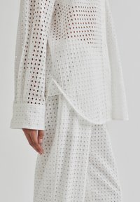 White top and pants made of textured, open-weave fabric featuring square patterns, with long sleeves and a curved hem.